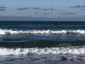 orilla de playa con oleaje y persona haciendo padel surf