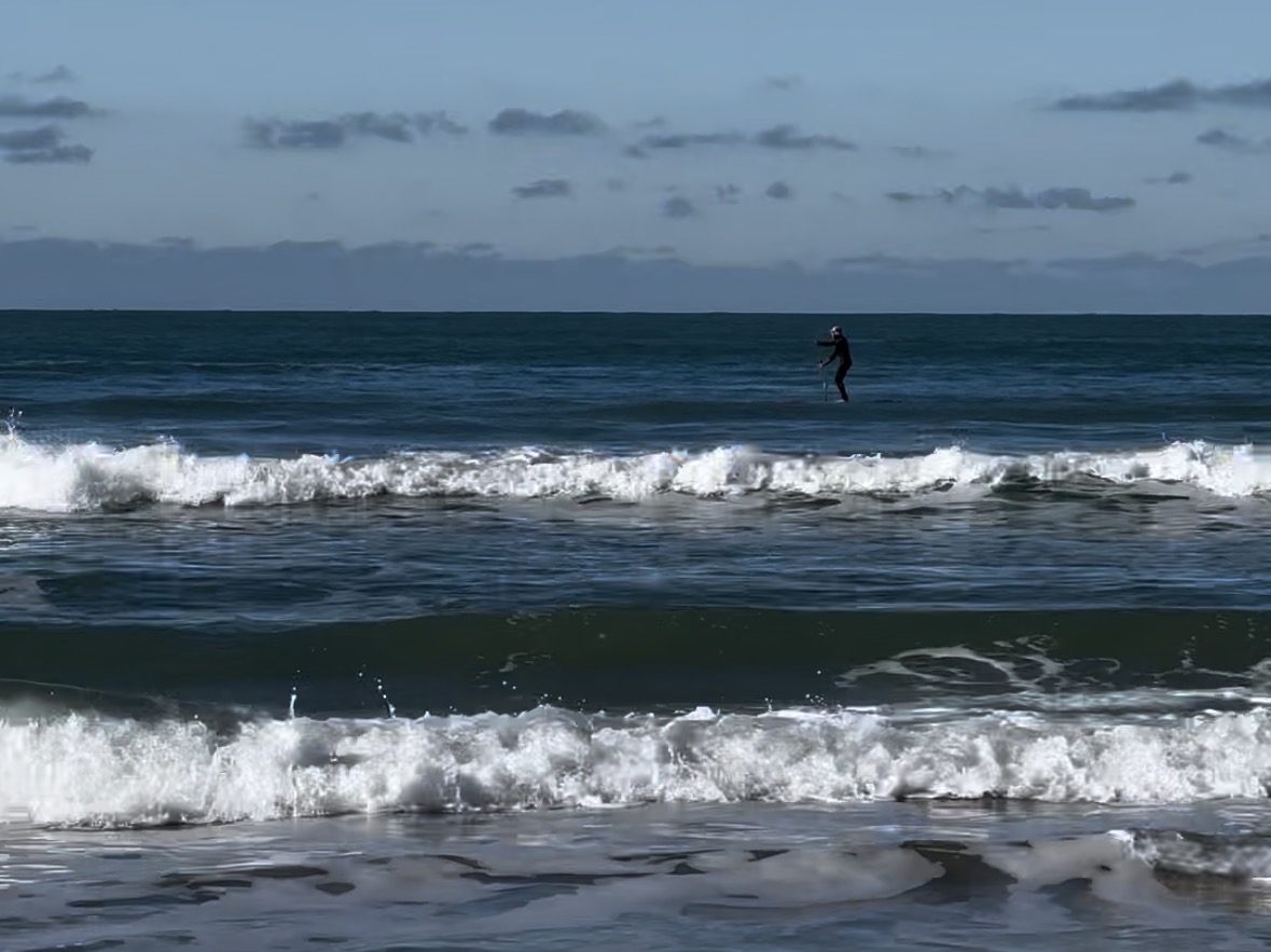orilla de playa con oleaje y persona haciendo padel surf